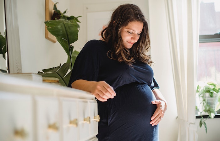 Smiling pregnant woman caressing tummy in house room - prenatal vitamins to get pregnant