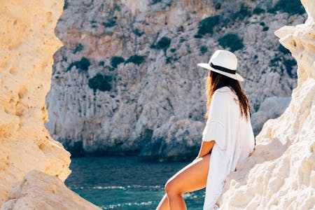 Last minute vacation deals woman relaxing against a rock face near the water